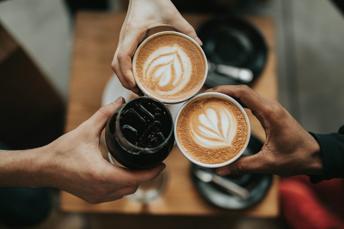 Three people holding coffee drinks together over a wooden table